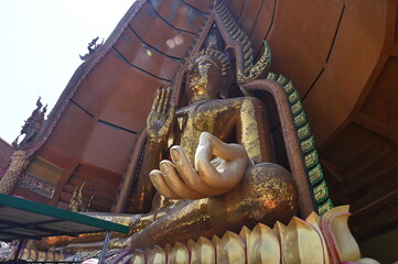 A large golden Buddha image in the blessing posture is enshrined on a hill. Along with a Thai-style...