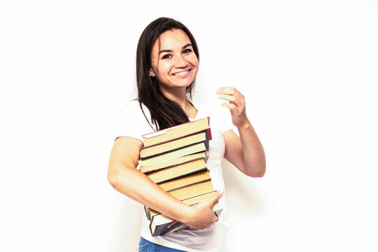 Young smiling student woman in white t-shirt holding textbooks and books in a pile on a white backdrop. College education concept. Positive emotions, facial expression