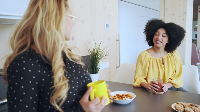 Video of two smart entrepreneur women talking while taking a break and having a breakfast in the kitchen at coworking place.
