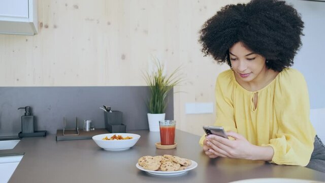 Video of beautiful afro woman sending messages with her smartphone while drinking tea in the kitchen at coworking place.