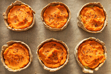 Rye homemade little pies pastry with carrot and potato filling on baking paper. Close-up, top view.