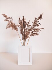 White frame mock up and dried natural pampas grass in white vase on bookshelf or table. Interior decoration element. Background boho. Minimalism design. Place for text. Selective focuson