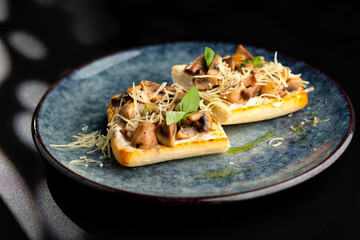 Bruschetta with mushrooms and tomatoes on a blue plate, on a black background.