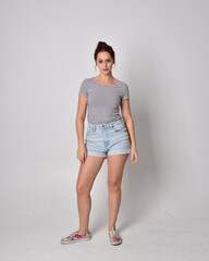 full length  portrait of girl wearing shirt and denim shorts. Standing pose isolated on grey studio...