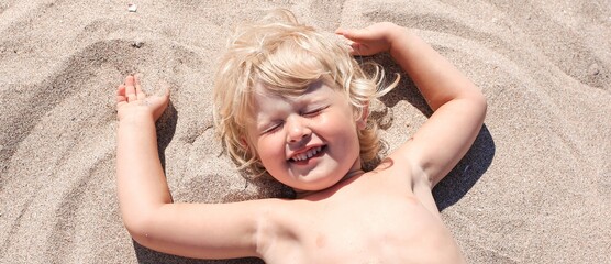 Little boy lying on the sand and playing on the beach of Mediterranean sea. Summertime, vacation, travel banner.	