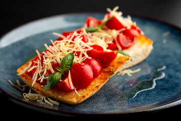 Bruschetta with mushrooms and tomatoes on a blue plate, on a black background.