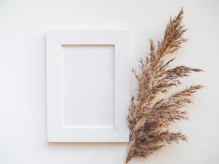 White frame mock up and dried natural pampas grass. Interior decoration element. Flatlay top view. Background boho. Minimalism design. Place for text. Selective focuson