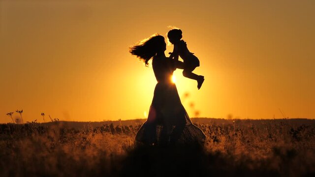Happy family child and mother playing together at sunset silhouette. people in the park concept mom daughter joyful whirl. happy mommy and little baby child fun summer kid dream concept, fly freely in