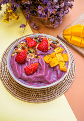Eating healthy breakfast bowl. Healthy food Acai breakfast superfoods smoothie bowl with chia seeds, bee pollen, fresh Strawberry, almond and granola for healthy vegan on color paper background