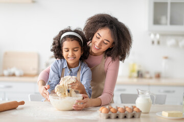 Happy black woman and girl preparing dough in kitchen