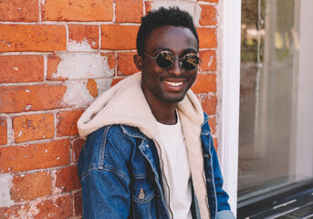 Portrait of stylish happy smiling young african man on a city street over brick wall background