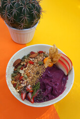 Close-up of Acai breakfast and  superfoods smoothie bowl with seeds, Strawberry, almond and granola for healthy vegan on color paper background