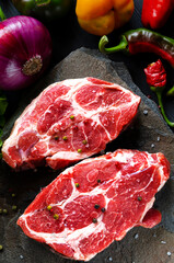 Meat raw steaks lie on a black background with vegetables, fresh blue onions, yellow peppers, chili. background image. side view, top view