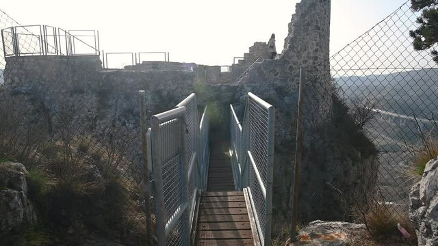 Narrow walk bridge connected with land, Crni kal fortress in Slovenia. Ruins of a castle overlooking Črni Kal village. Famous historic site. Tilt up, wide angle