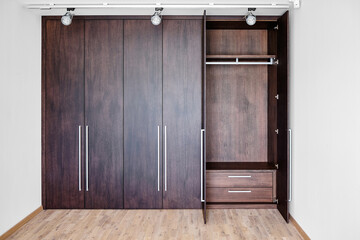 Open doors of elegant wardrobe with inner drawer made of dark oak veneer with shiny metal handles...
