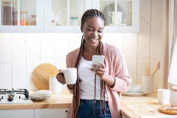 Hapy Black Lady Drinking Morning Coffee And Using Smartphone In Kitchen