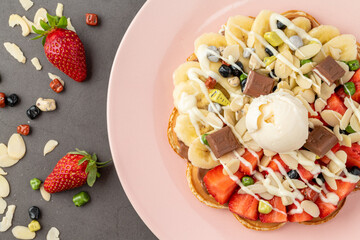 Heart waffle with banana and strawberry with gummy candy and ice cream on it.