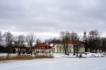 in the spring with ice on which you can see the footprints of cars, with light blue skies and dark trees, and some stone buildings.