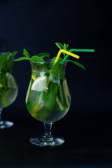Summer mint lime refreshing cocktail mojito with rum and ice in glass on black background. Mojito cocktail on dark stone table. Glassy high glass for drinks. Lemonade at the bar.