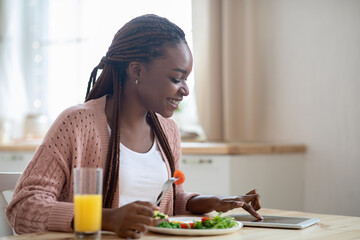 Smiling Black Female Using Digital Tablet While Having Breakfast In Kitchen