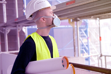 young male builder foreman, worker or architect in white hardhat and protective respirator during...