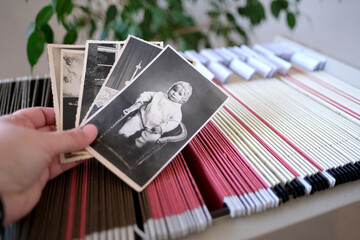 hands hold a stack of vintage photographs lies on an archival metal cabinet with thin files with...