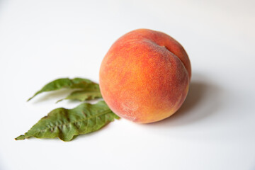 Ripe natural peach with a leaf on a white table. Healthy eating, seasonal fruit and diet concept.