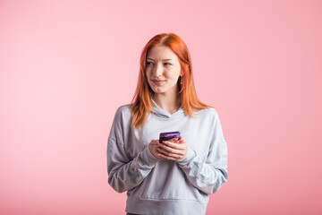 Dreaming redhead girl with phone in studio on pink background