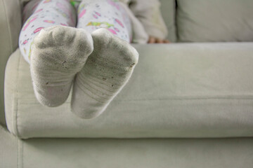 Little girl sitting on sofa in dirty socks