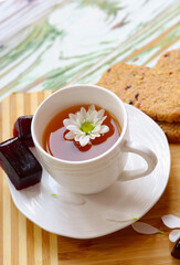 Flat lay chamomile tea in a white cup on a saucer where a wooden substrate and decor are book and flowers. Sweets. Marmalade. Morning concept