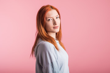 Portrait of a satisfied redhead girl in the studio on a pink background