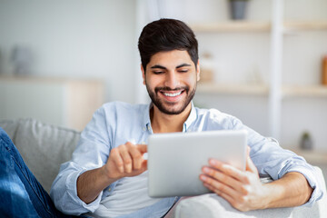 Happy arab man using digital tablet, shopping online, browsing internet or working remotely on tab computer