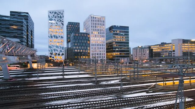 Train Leaving Oslo Central Station With Barcode Project Buildings At Night In Bjorvika, Oslo, Norway. - wide shot