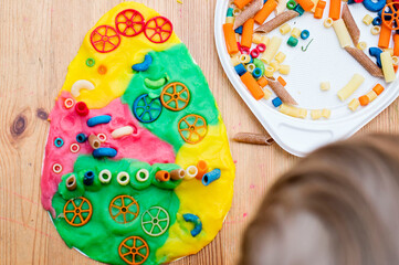 Easter concept. the child places colored noodles on an egg-shaped plasticine. children DIY toys for home ideas, child employment, fine motor skills, ergotherapy, sensory therapy