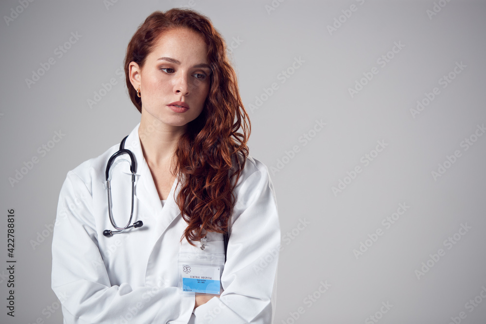 Wall mural Studio Portrait Of Stressed Young Female Doctor Wearing White Coat Against Plain Background