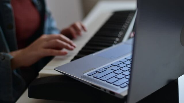 Close-up of female hands on the electric piano. A woman is learning to play the synthesizer on a laptop