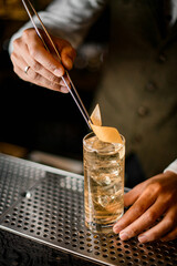 male bartender neatly decorates glass with cold drink by orange zest using tweezers