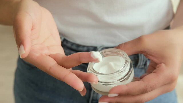 Black african american woman hand taking a white moisturize cream from jar her finger. Skin care routine with organic beauty natural cosmetic.