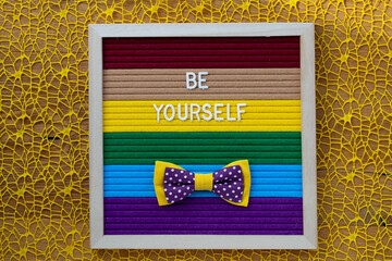 Words BE YOURSELF with red bow on rainbow surface. Closeup