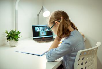 Little school girl having virtual lesson at home using laptop during homeschooling at pandemic quarantine