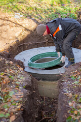 A worker installs a sewer manhole on a septic tank made of concrete rings. Construction of sewage...