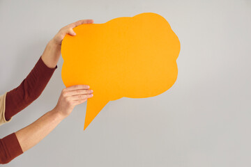 Unrecognizable faceless person holding amber orange mockup copyspace speech bubble in hands on gray background. Blank space to share message, express opinion, spread word, advertise and promote idea
