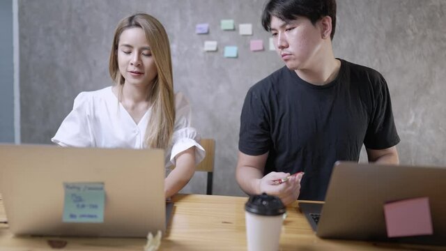 ํYoung handsome man spying on female colleague who is working at laptop, looking at her computer screen, taking curious glance, cheating on exam, stealing idea or information, competition and gossip