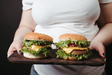 Obese woman with two tasty fattening hamburgers