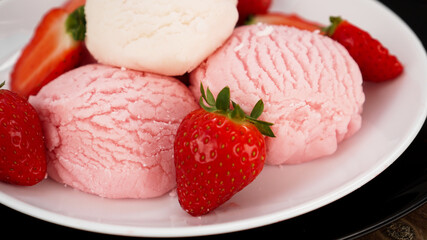 Delicious strawberry ice cream with fresh strawberrieson a white and black plate
