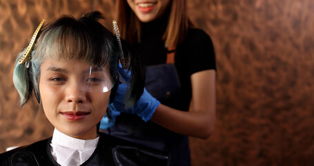 Professional Asian hairdresser dyeing hair of her client at beauty salon shop