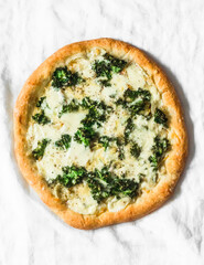Vegetarian potato, kale, mozzarella pizza on a light background, top view