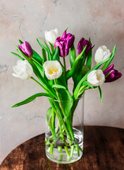 Bouquet of colorful tulips in a glass vase on a wooden table. Home interior decorating