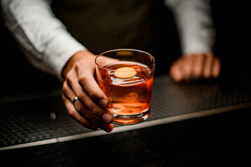 male bartender holds in his hand old-fashioned glass with cold alcoholic cocktail
