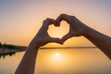 Forming a heart shape with two hands in front of a beautiful sunset